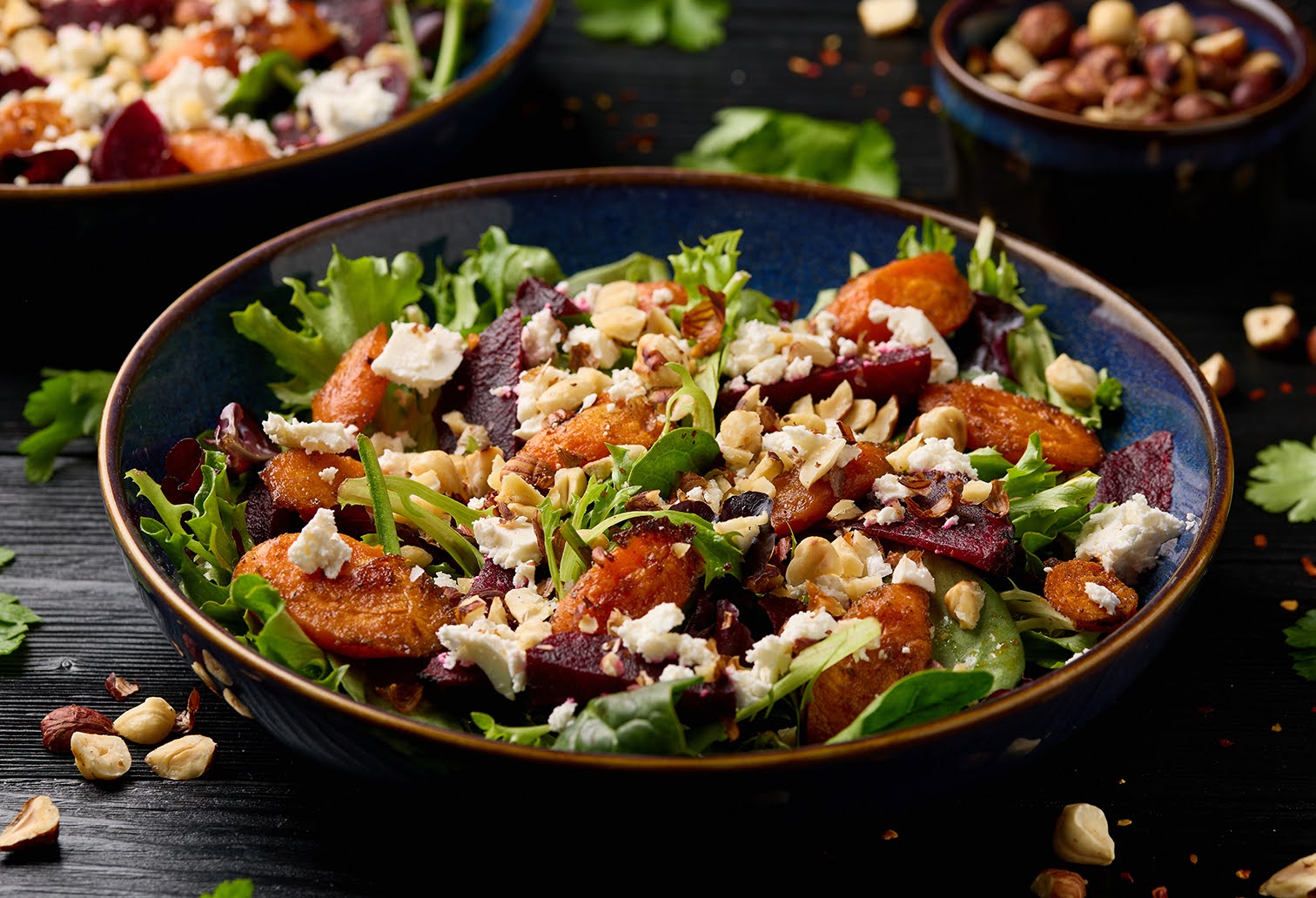A bowl of crispy greens with roasted beets and carrots, topped with crumbled cheese and nuts