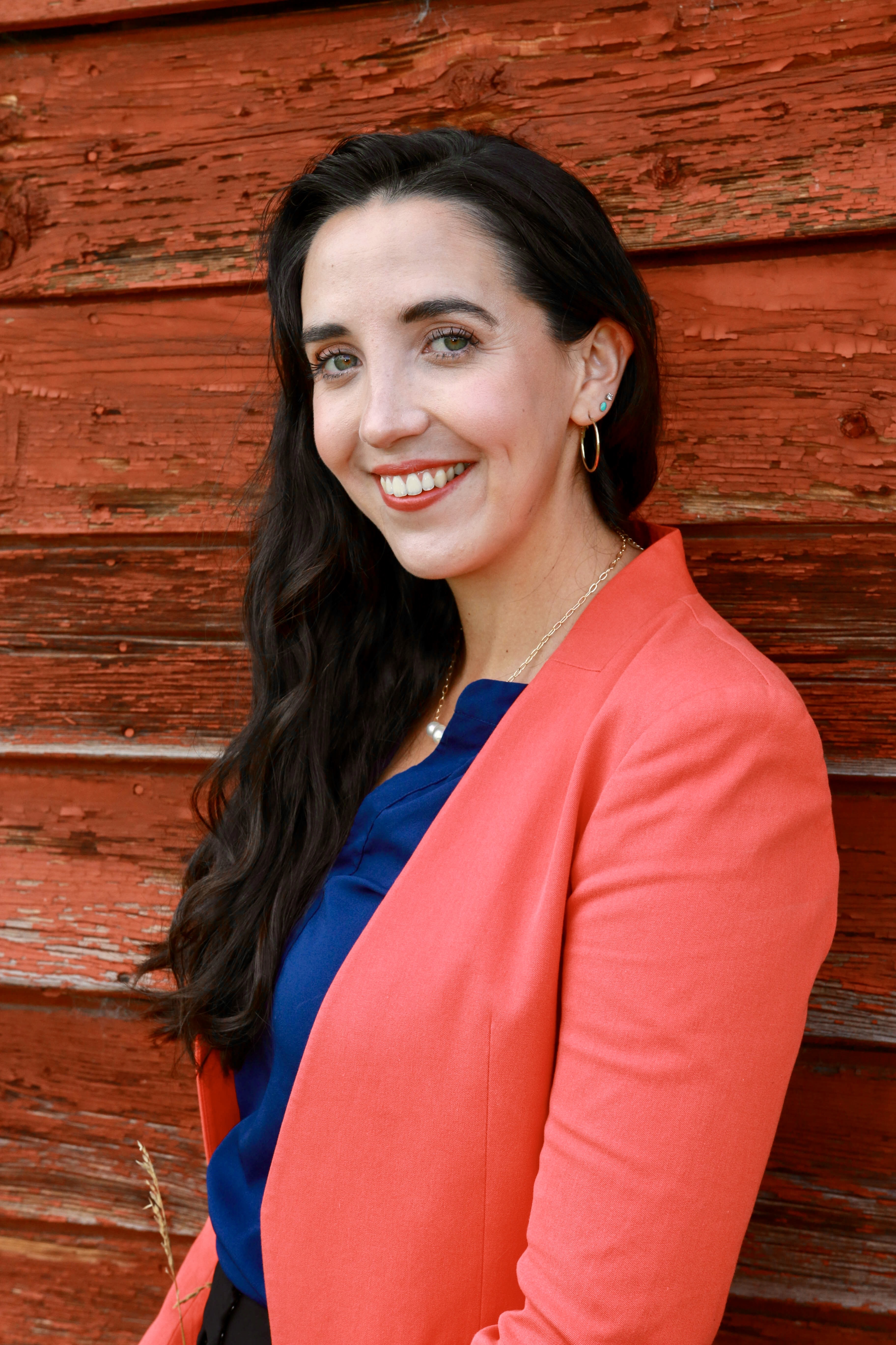 Evanne stands in a pink jacket in front of a red wooden building