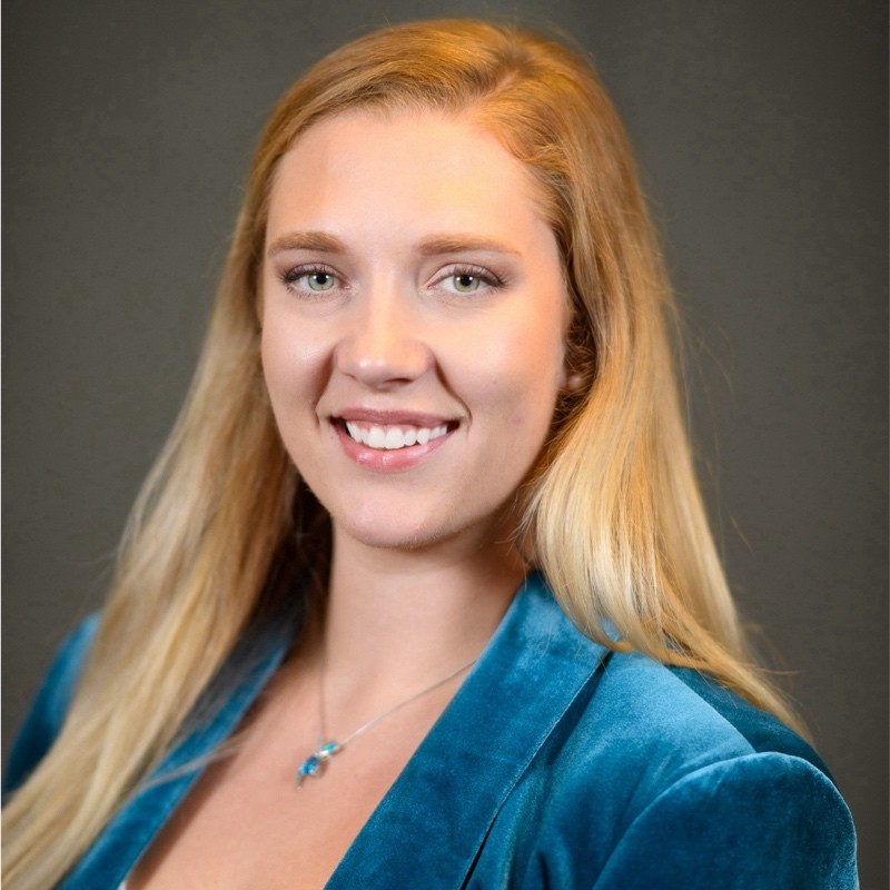 Headshot of Liz Thomas, she wears a blue jacket and smiles at the camera