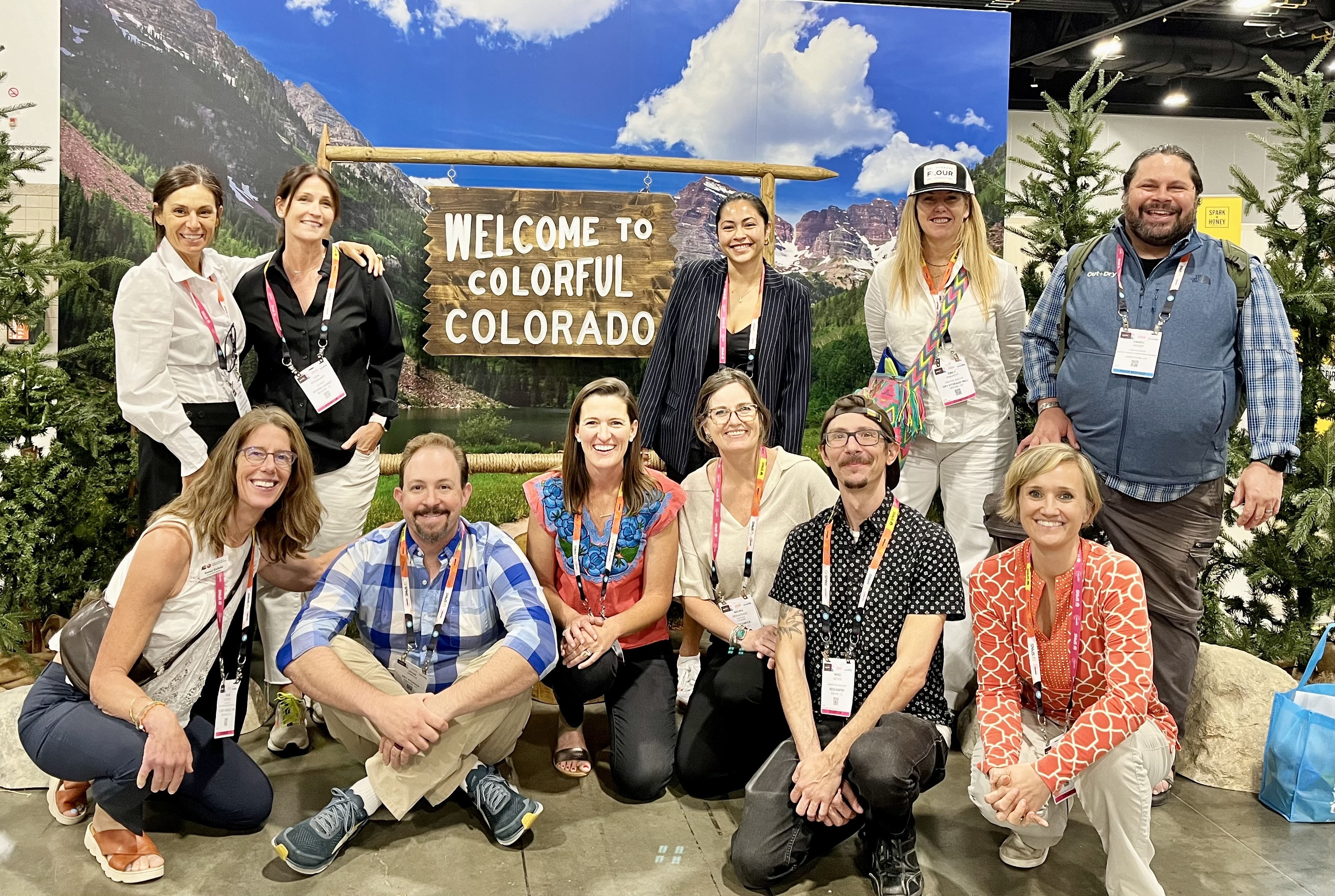 Exhibitors in the Colorado Climate Smart Showcase at Newtopia Now 2024 pose in front of a sign that reads Welcome to Colorful Colorado