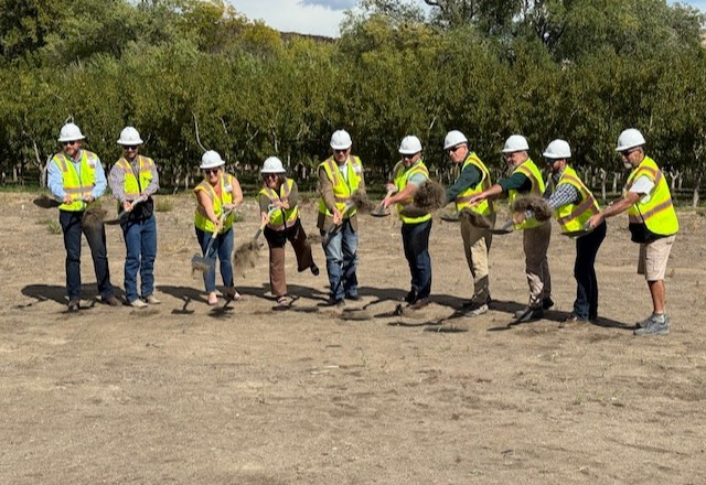 Ten people wearing hi-viz vests and hardhats, throw dirt off their shovels