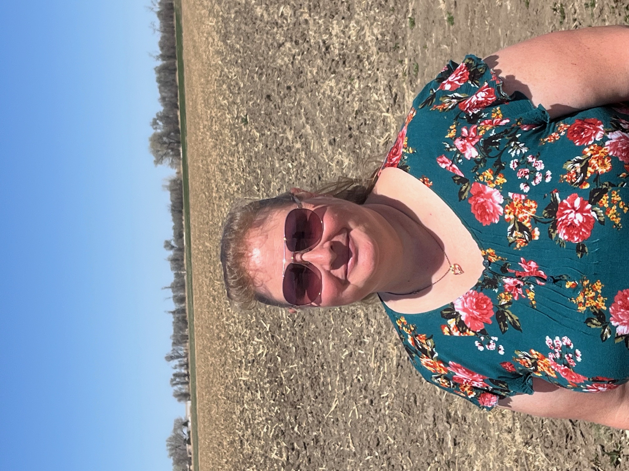 Michelle has sunglasses on and stands in front of a plowed field.