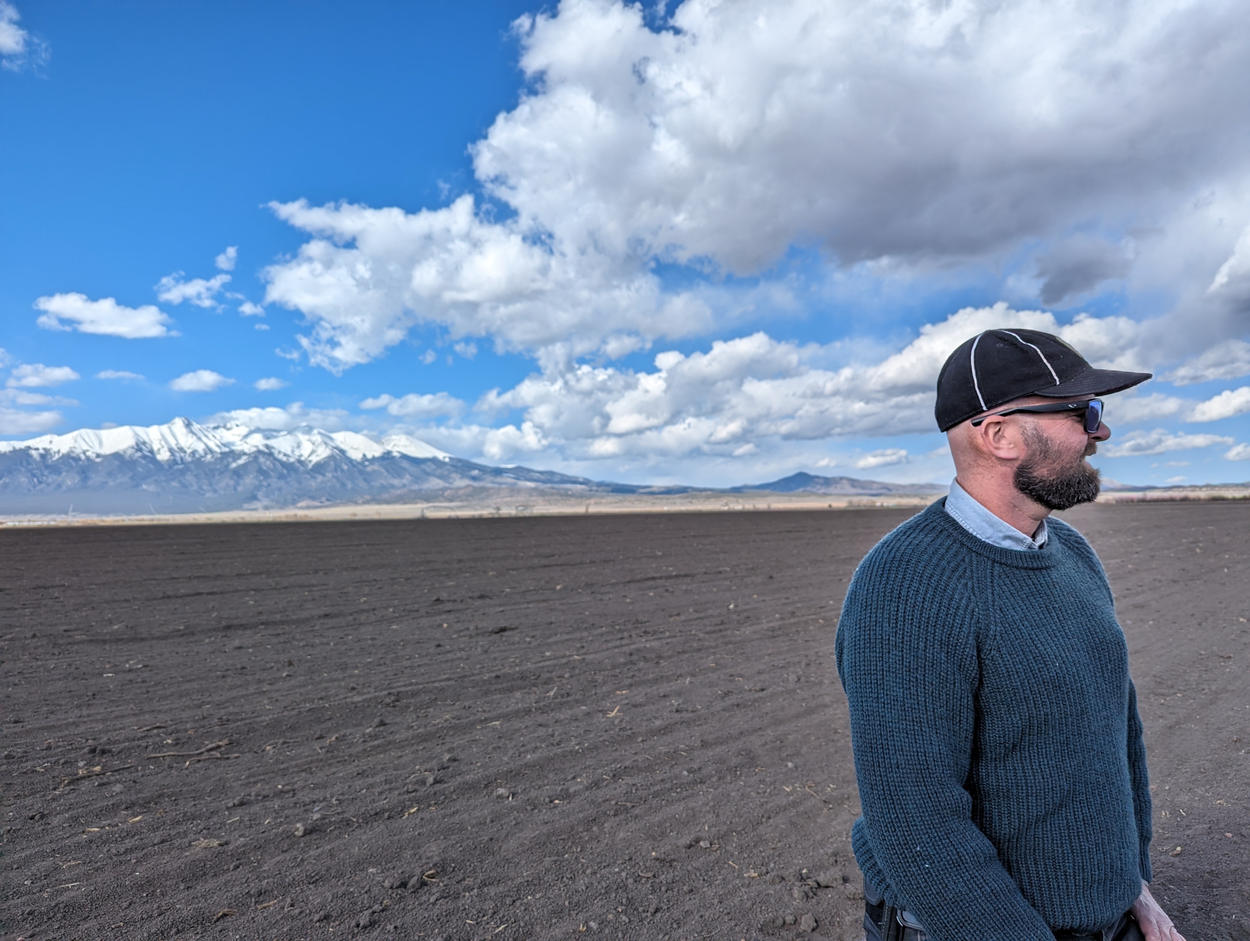 Toby stands in a bare field with mountains behind him. 
