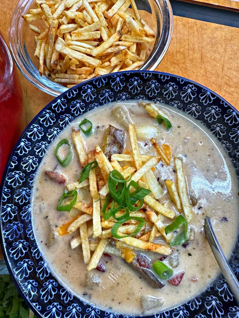 A bowl of potato bacon chowder garnished with french fries and green onions