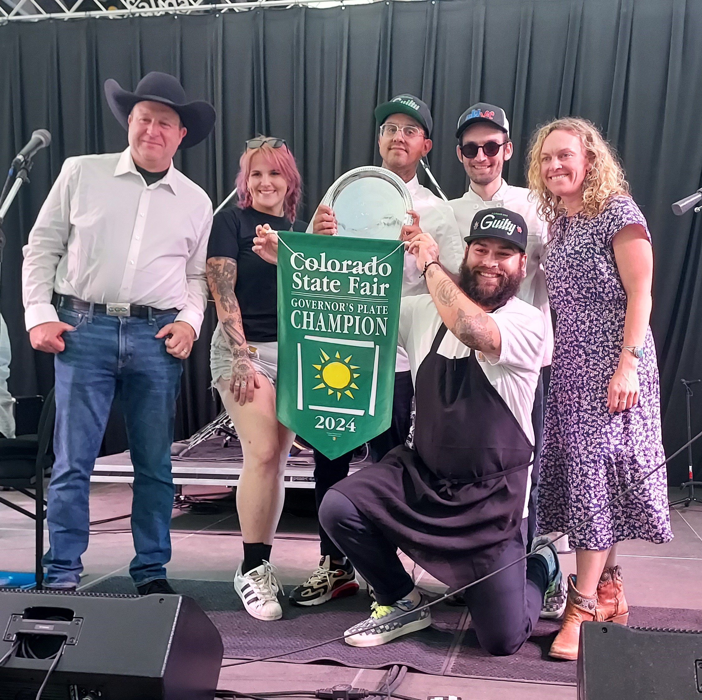 Governor Polis and Commissioner Greenberg present the Governor's Plate Champion banner to the chefs of Proto Taste food truck 