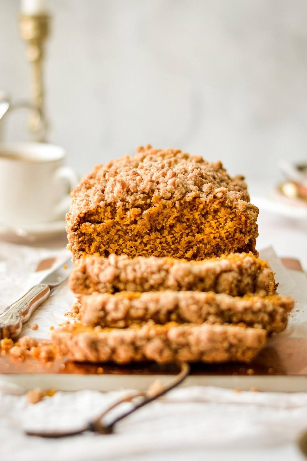 Three slices of a crumbly pumpkin bread fall decadently away from the loaf