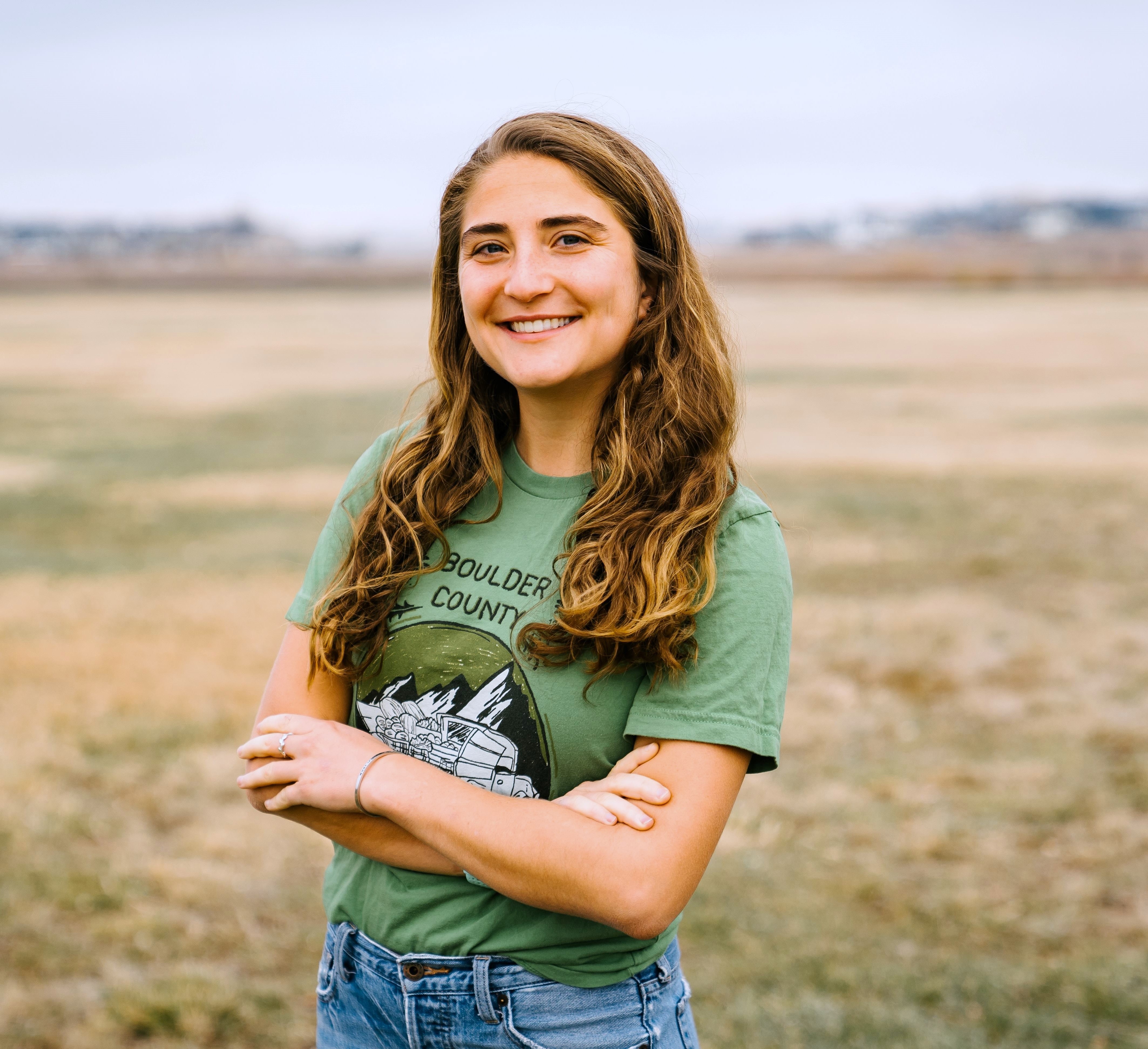 Rosie is standing in a green t-shirt with a field behind her. 