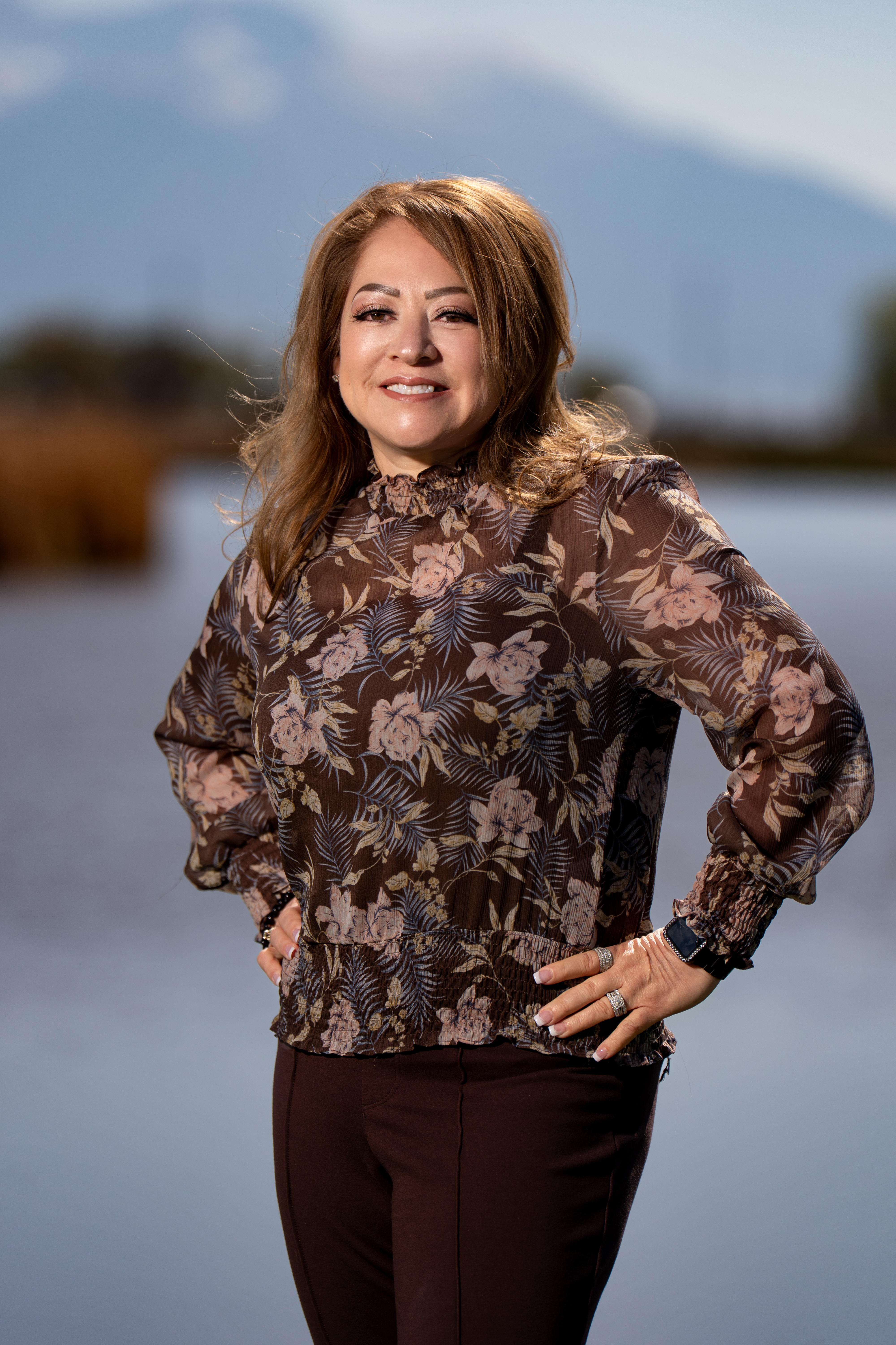 Leova stands with her hands on her hips in front of a blurred background. 