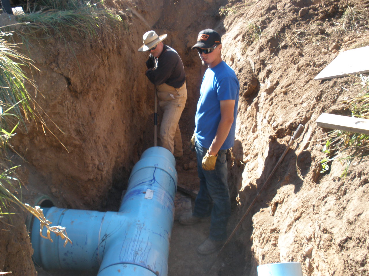 Two men work in a manmade ditch around a large blue water pipe