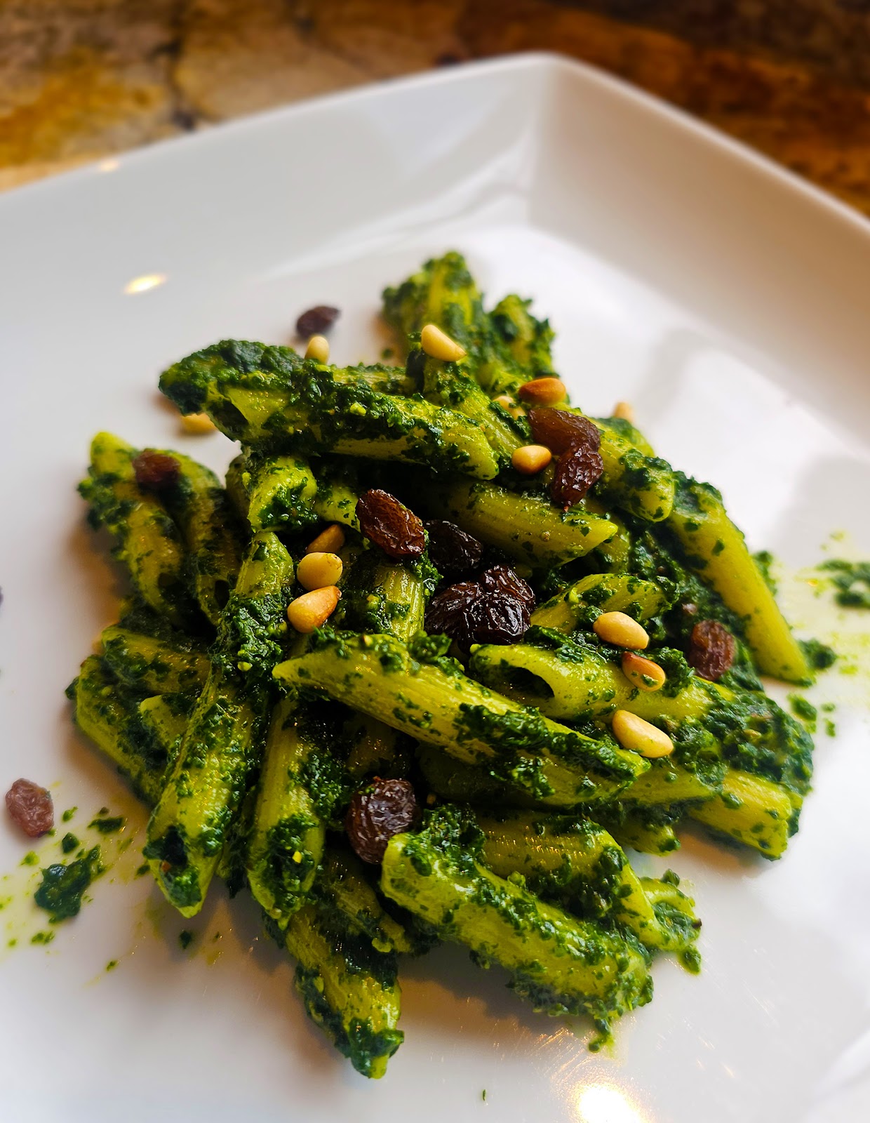 Penne pasta covered in vibrantly green spinach pesto and topped with pine nuts and raisins