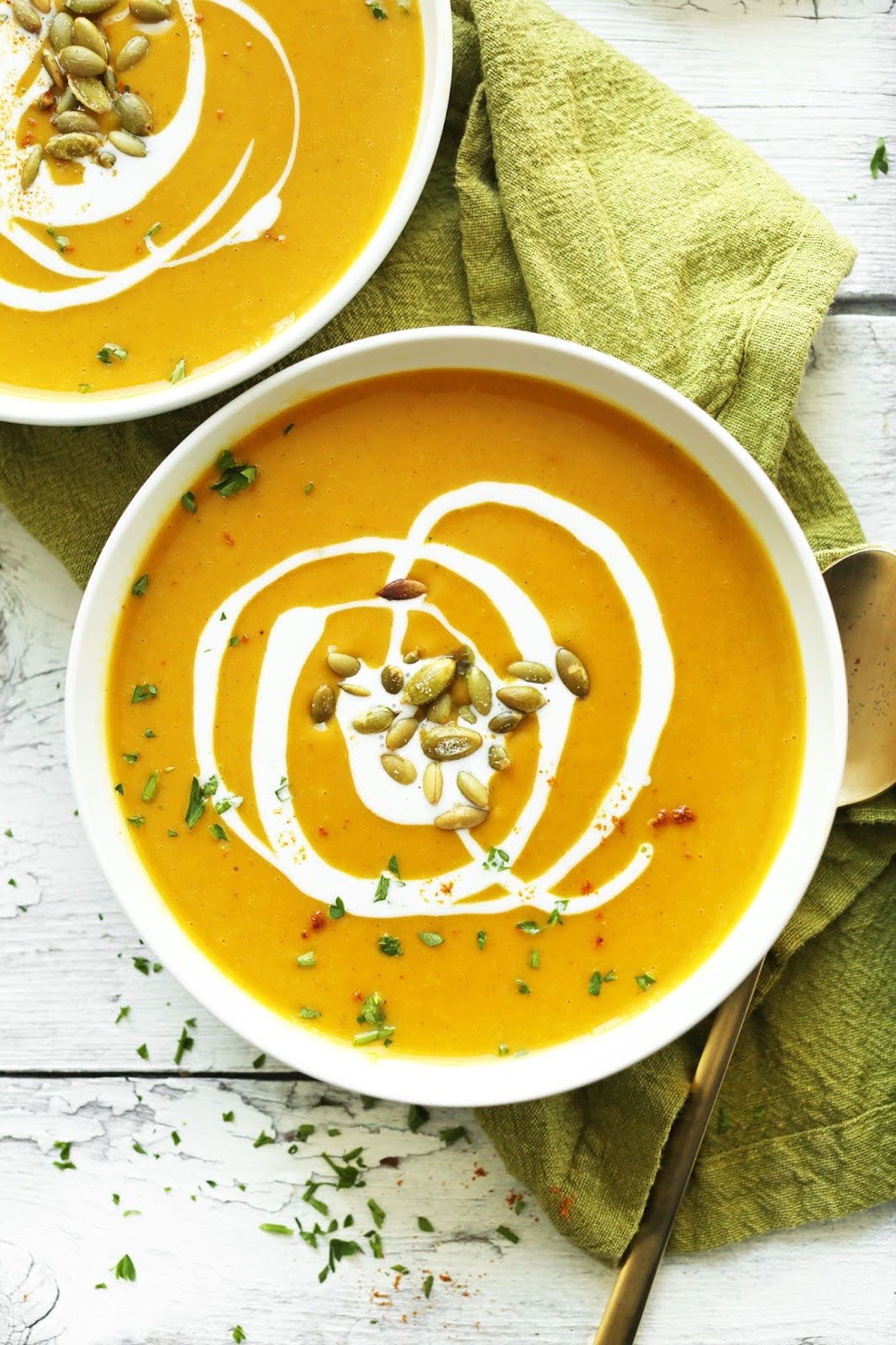 Closeup of two bowls of orange soup drizzled with cream and garnished with pepitas