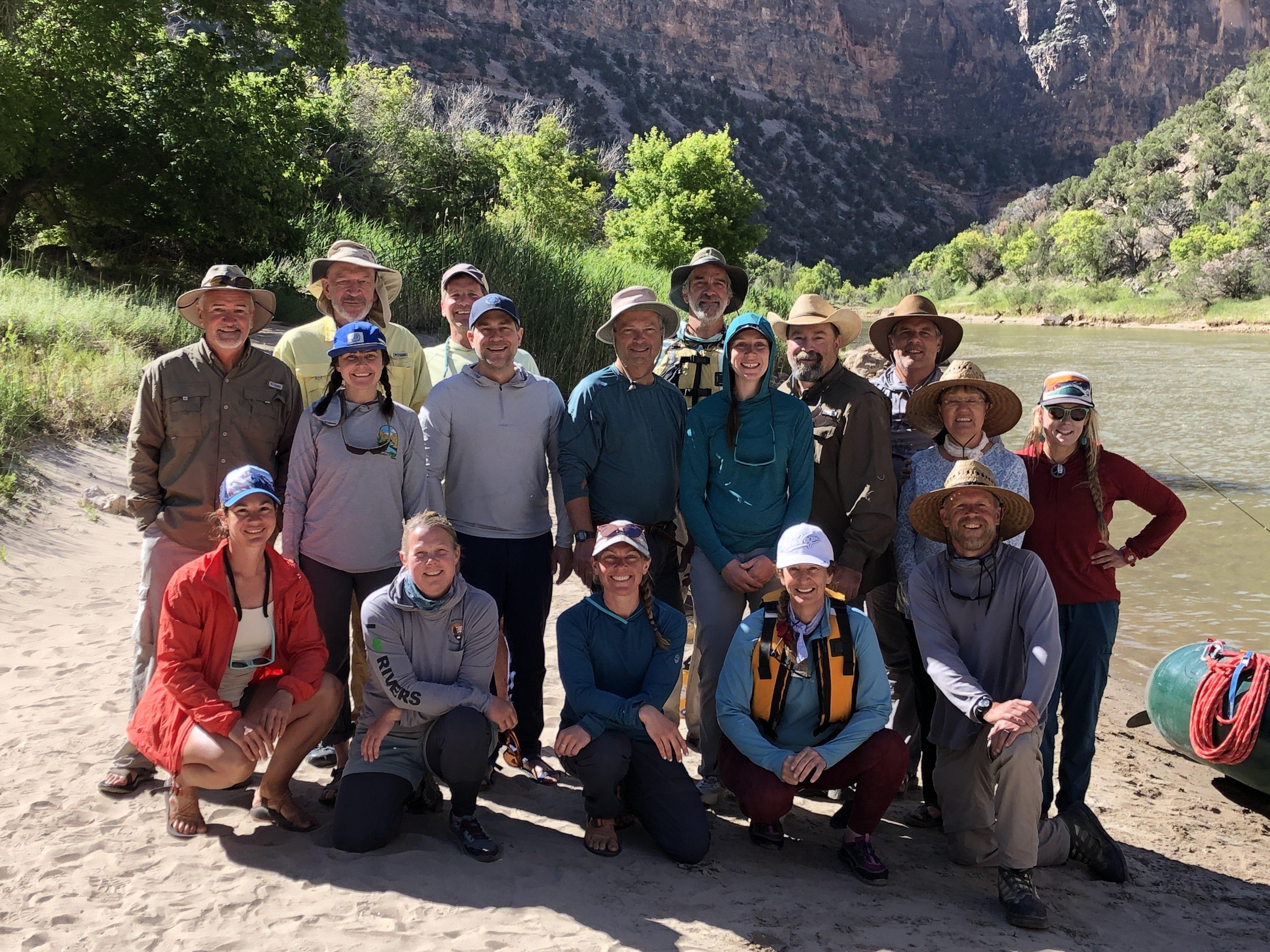 Group picture of men and women along the banks of the Green River in rafting attire..
