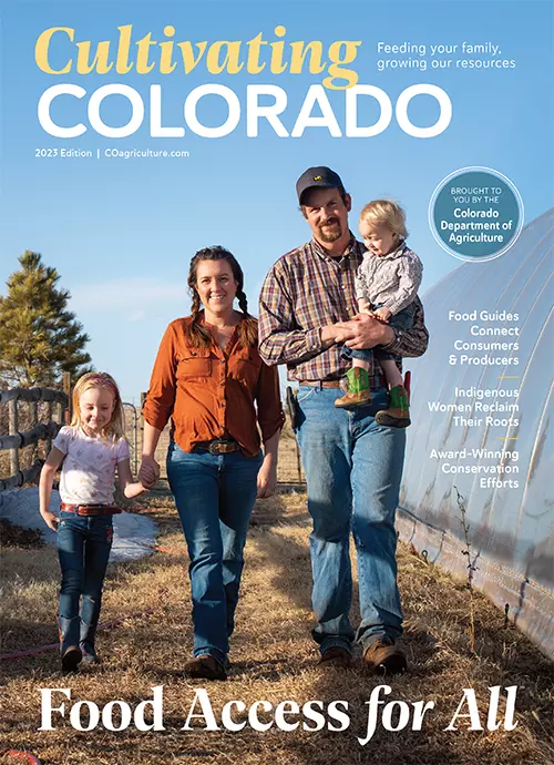 Young family walking, mom holds hands with an older daughter and dad carries the toddler in a farm setting next to a covered agricultural tunnel.