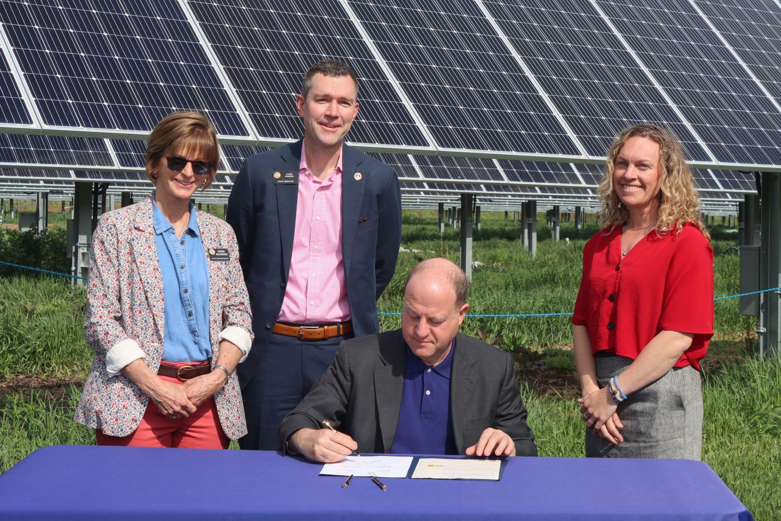 Colorado State Representative Karen McCormick, CO State Senator Chris Hansen, Agriculture Commissioner Kate Greenberg stand in agrivoltaic solar garden while Governor Jared Polis signs Senate Bill 23-092