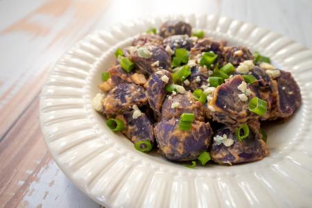 Roasted Colorado purple potatoes in dressing and garnished with green onion and blue cheese crumbles