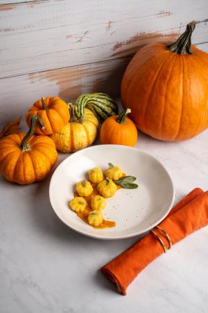 Pumpkin shaped and flavored gnocchi plated with sage browned butter sauce plated in a small bowl with seasonal gourds in the background