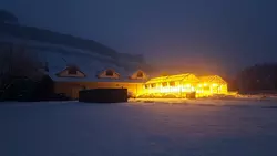 The transparent Palisade Insectary greenhouse building shines bright from within and illuminates the snowy night.