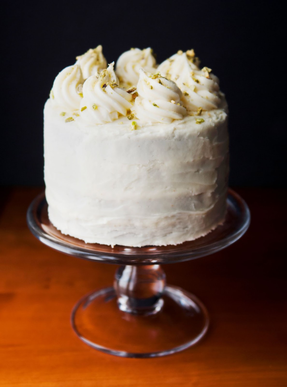 Frosted three layer carrot cake sits on a glass serving platter